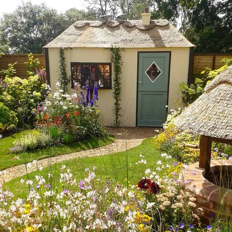 A quaint cottage with a thatched roof, surrounded by a vibrant garden of flowers and greenery, under a clear sky