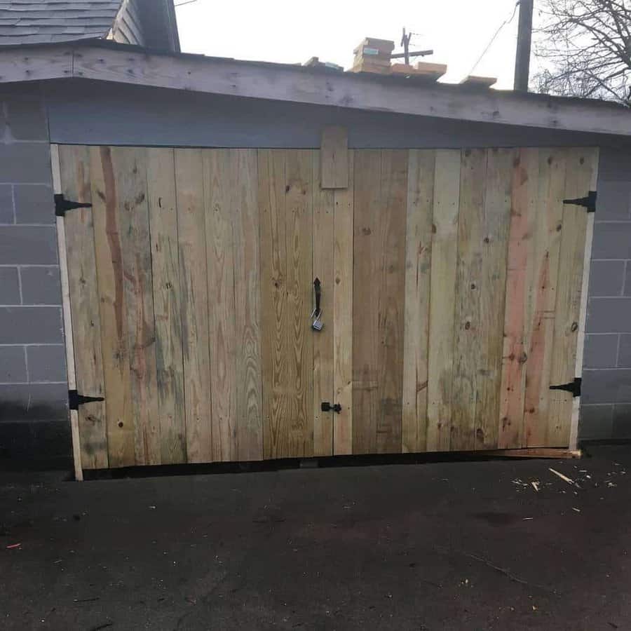 Rustic double shed doors made of raw vertical wooden planks with black hinges and a padlock, set against a cinder block structure