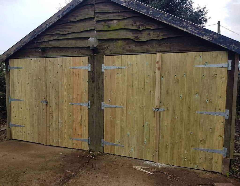 Large wooden shed with two sets of double doors made of fresh vertical planks, secured with silver metal hinges and latches