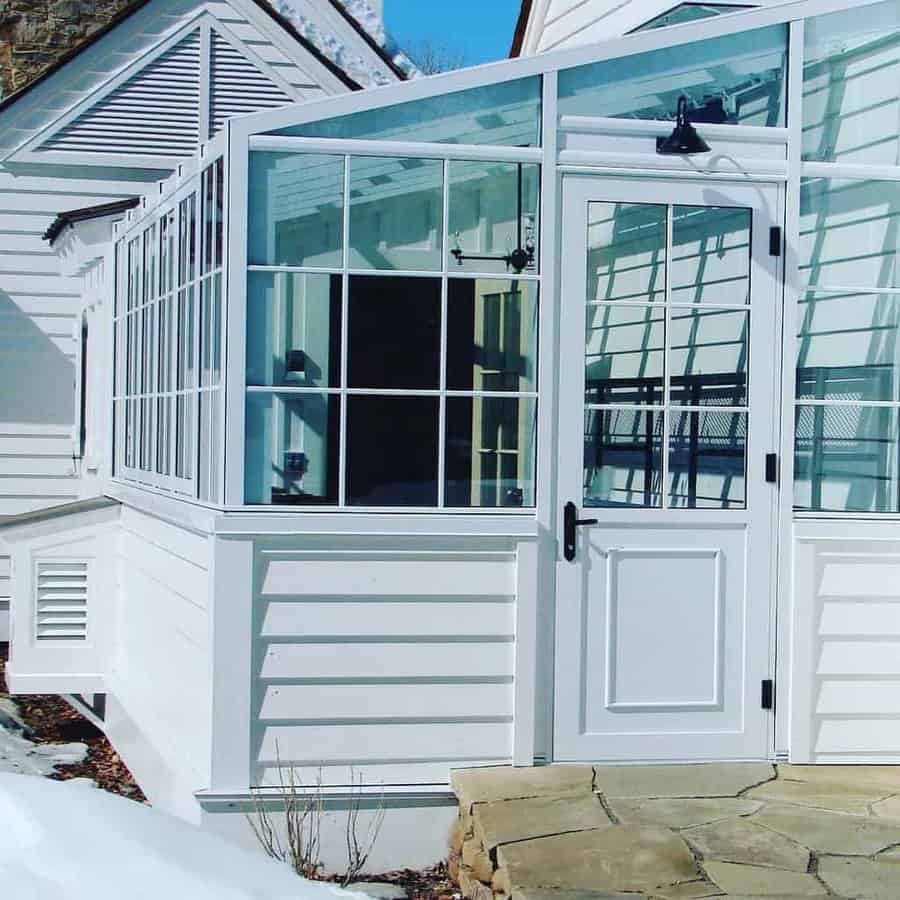 White greenhouse with glass panels and a door attached to the house