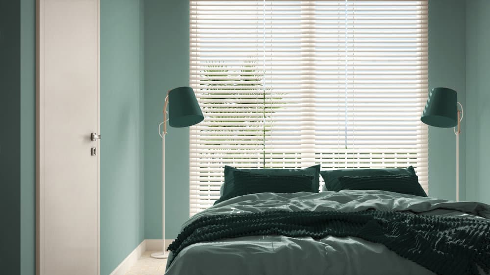 Chic bedroom with teal walls, blinds, and matching lamps