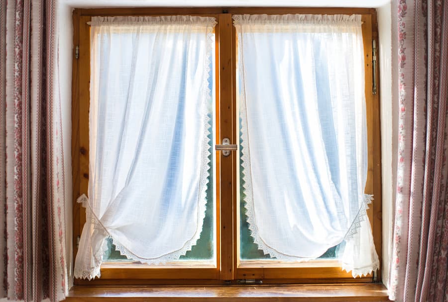 Rustic window with sheer lace curtains and sunlight