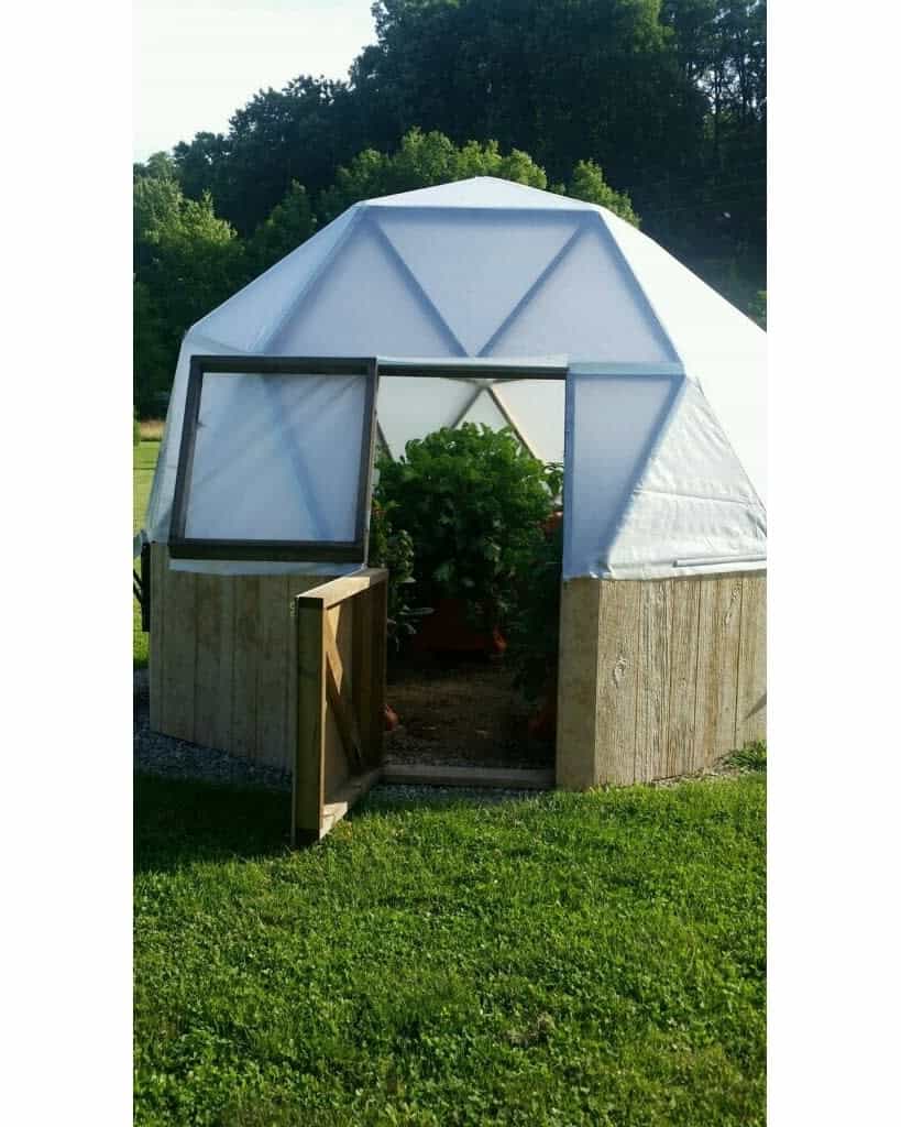 Dome greenhouse with open door in a grassy field