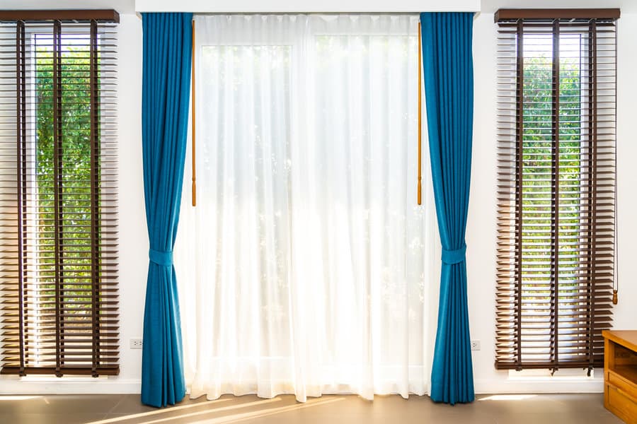 Sheer curtains with blue drapes between wooden blinds