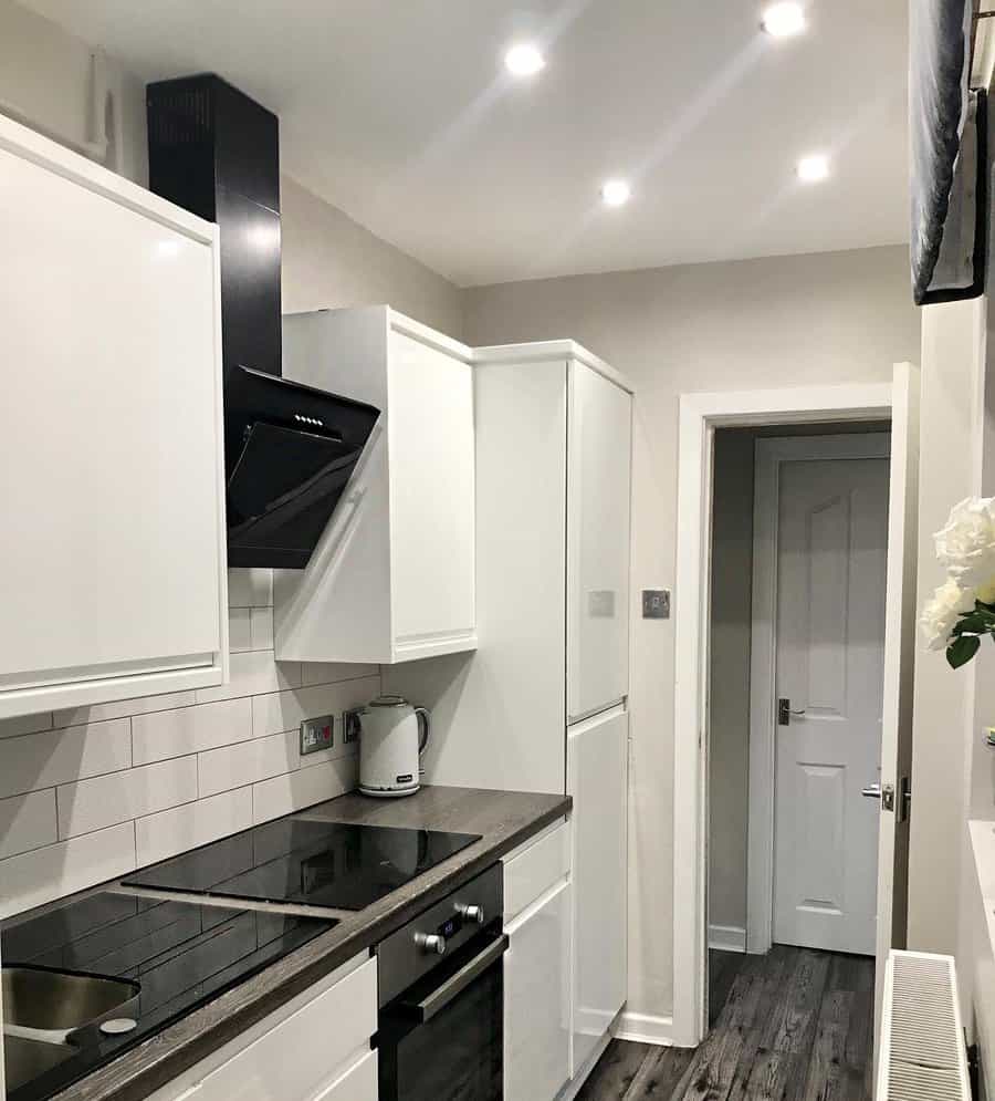 Narrow kitchen with white cabinets and grey subway tiles