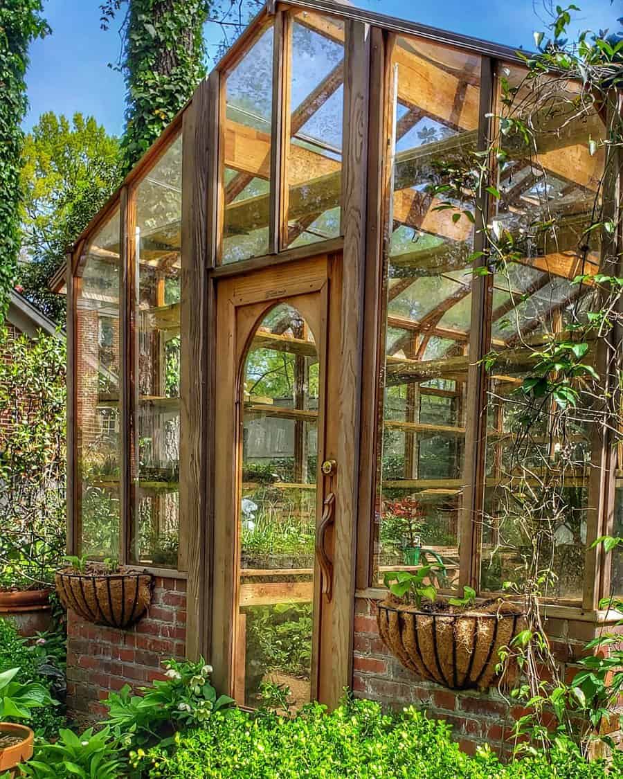 Tall wooden and glass greenhouse with lush surroundings