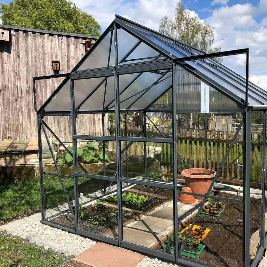 Metal greenhouse with an open vent in a rustic garden setting