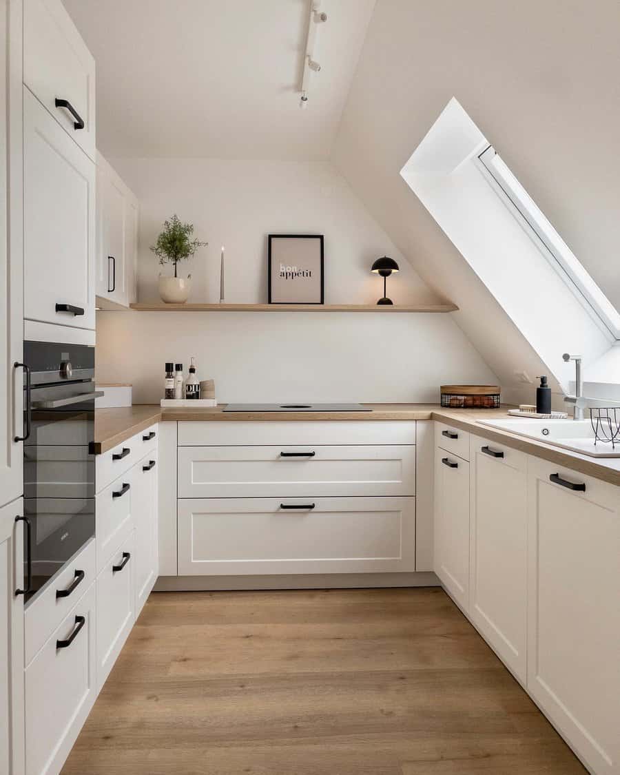 Minimalist attic kitchen with white cabinets and wood floors