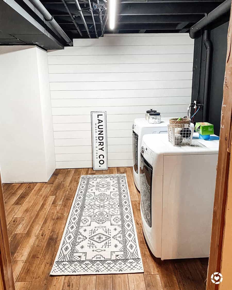 Stylish laundry room with white washer and dryer, patterned rug, wooden flooring, and a "Laundry Co" sign on the wall