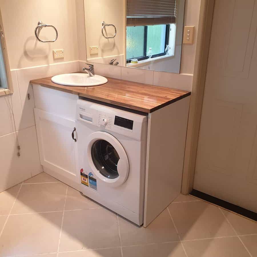 Laundry area with a front-loading washing machine, wooden countertop, sink, and wall mirror above an under-sink cabinet