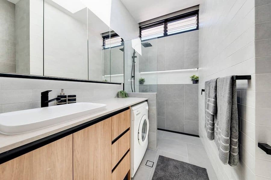 Modern bathroom with light wood cabinetry, a washer, glass shower, gray towels, and a large mirror