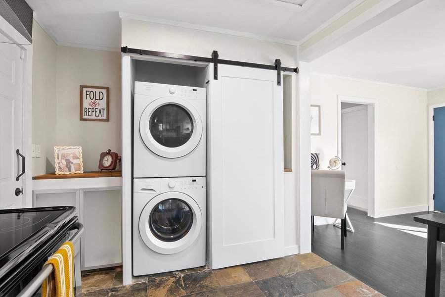 Laundry area with white stacked washer and dryer behind a sliding barn door next to a countertop with decor and a sign