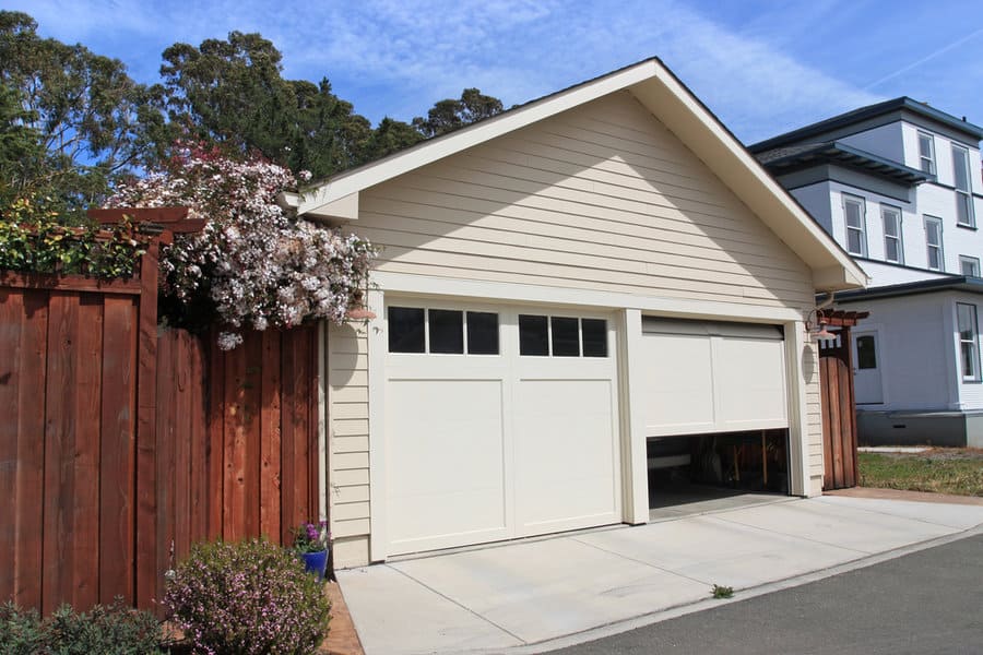 Partially open double garage door with blooming shrubs