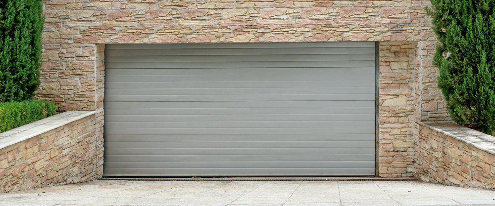 Grey roll up garage door with stone wall and shrubs