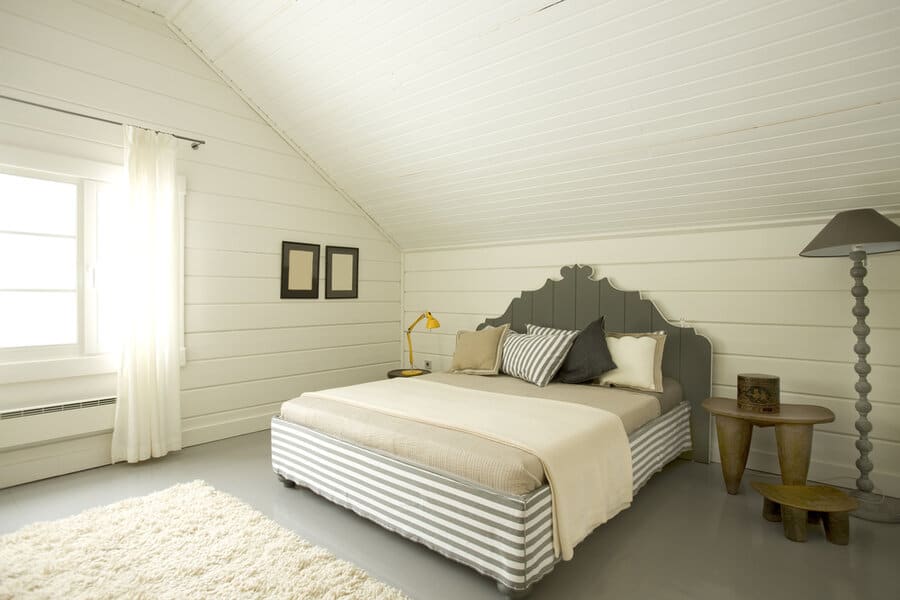 Bright attic bedroom with white paneling and striped bed