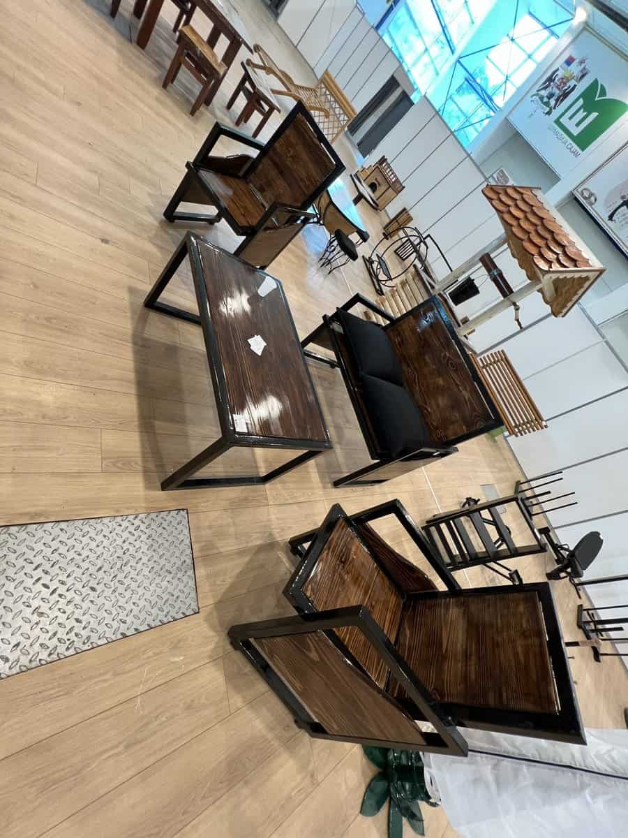 Exhibition room displaying wooden furniture, including chairs, tables, and a swing; light wood flooring and bright natural light