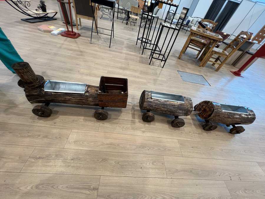 Wooden log train planter with three log cars on wheels displayed on a light wooden floor indoors