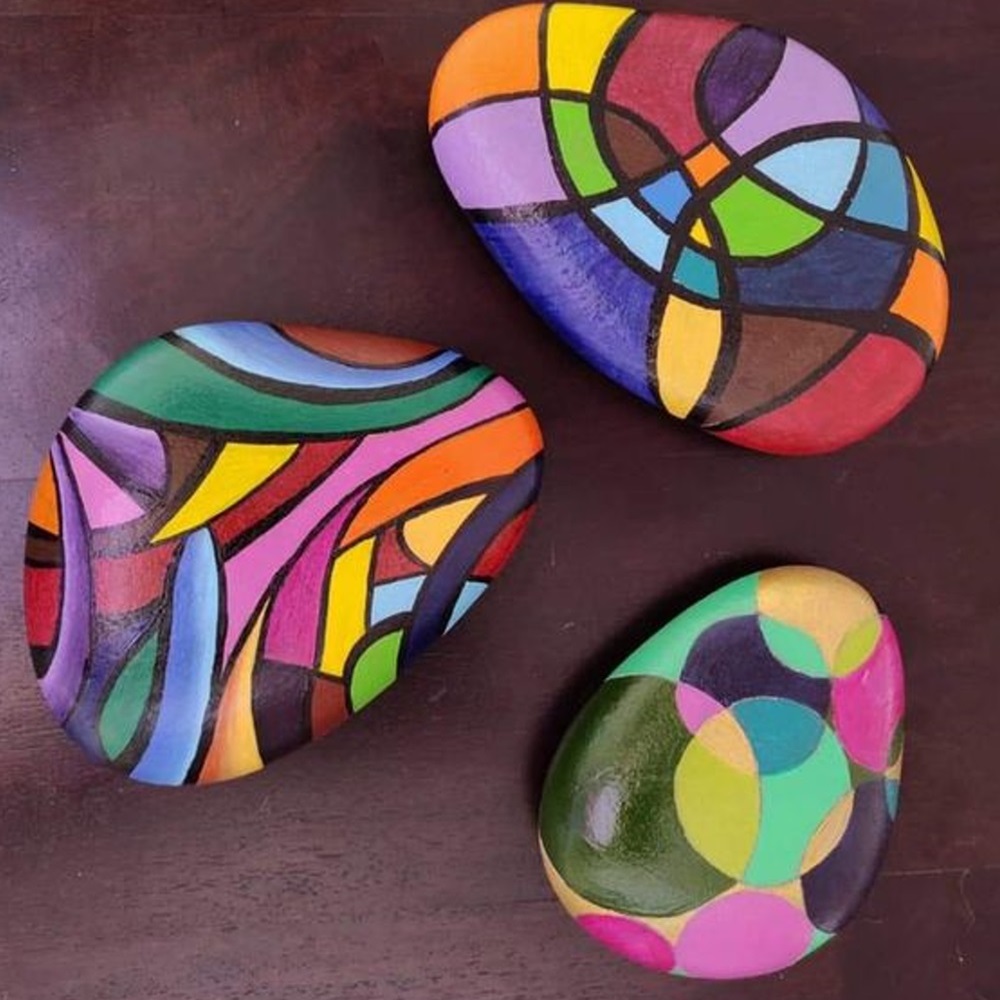 Three rocks with colorful, abstract designs painted on a dark surface