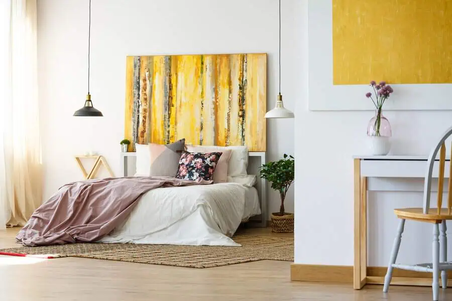 Bright bedroom with yellow and white decor, abstract headboard artwork, and cozy bedding.