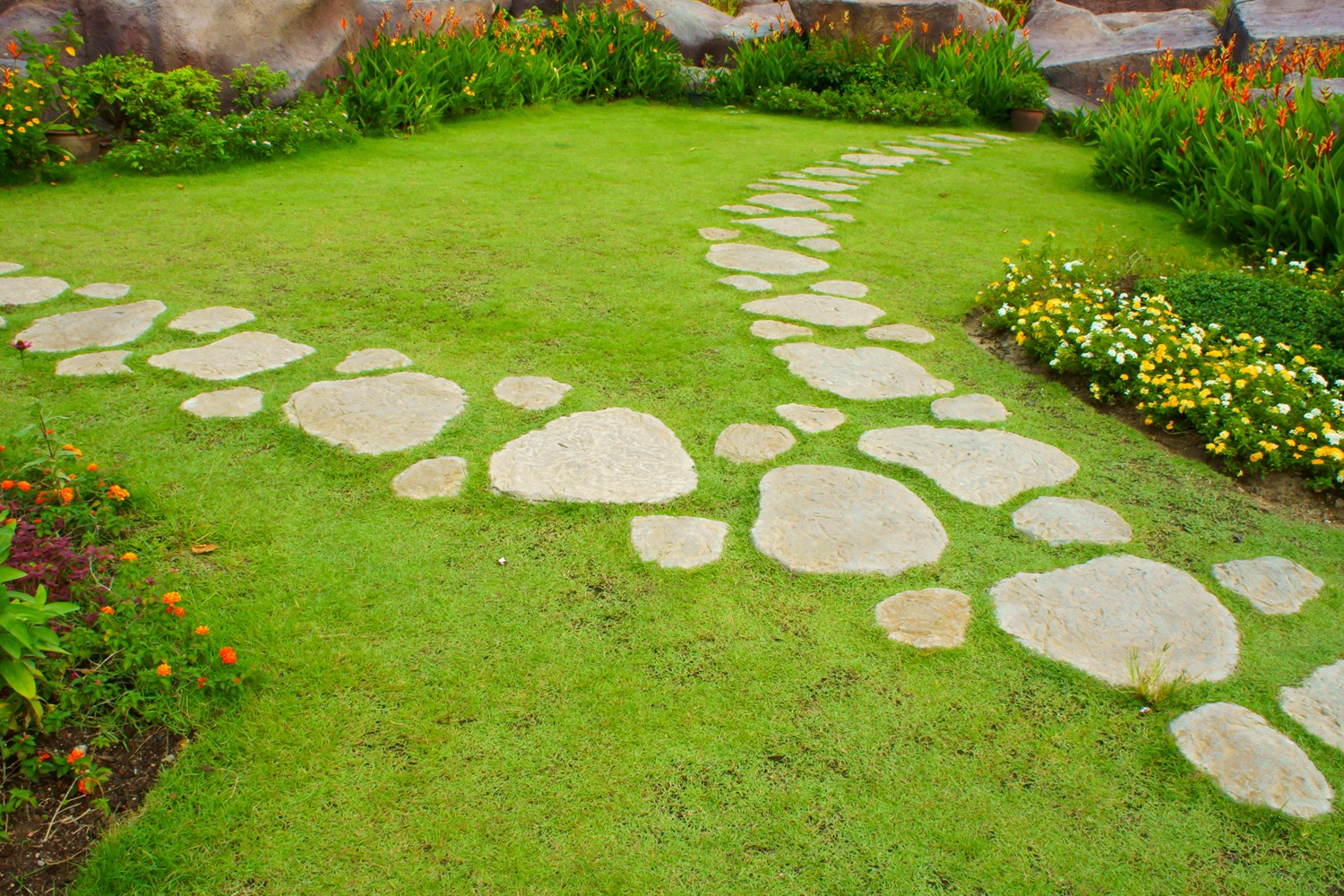 Stone path winding through a lush green garden with colorful flowers on both sides