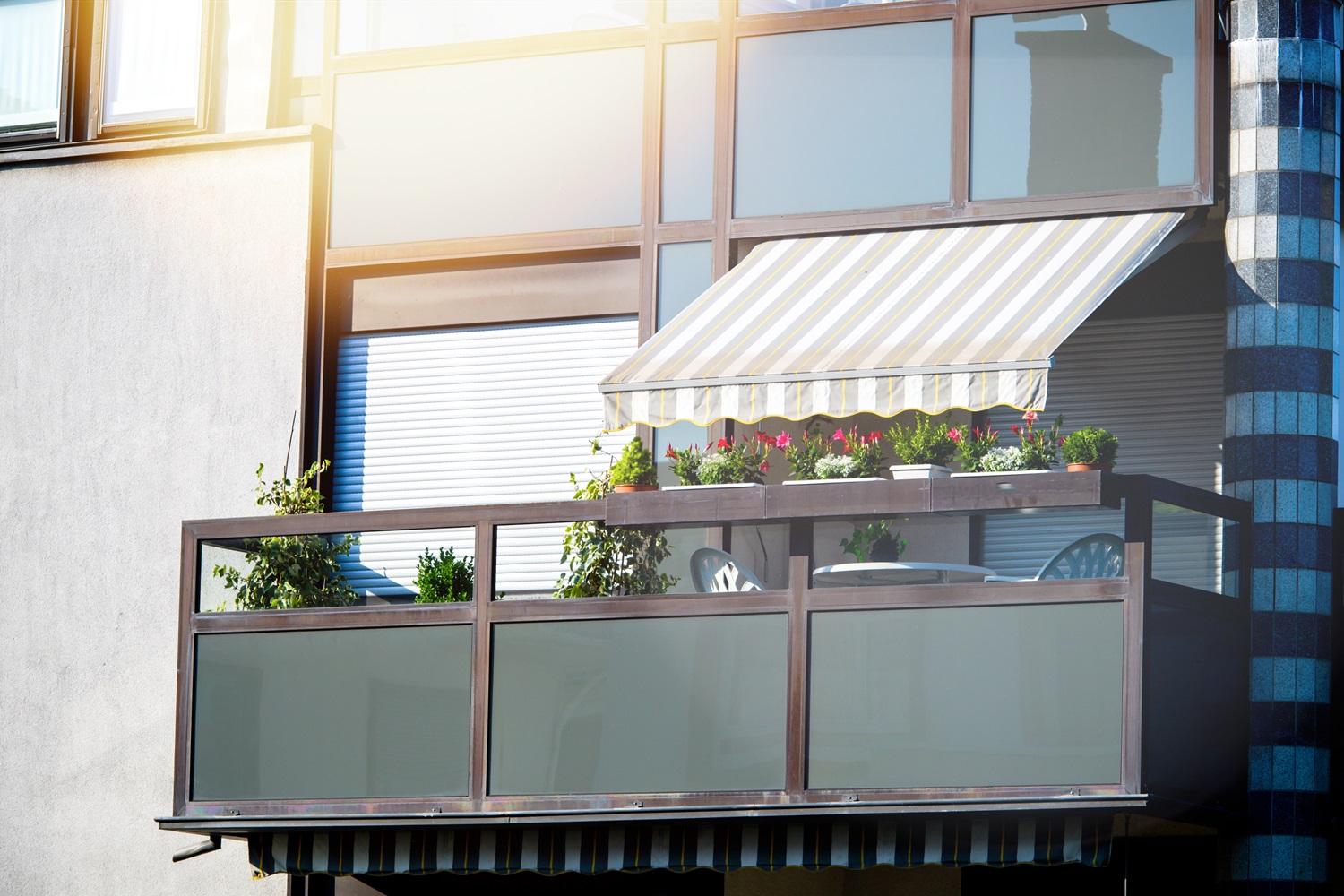 Balcony with plants, flower boxes, striped awning, and a small table with chairs