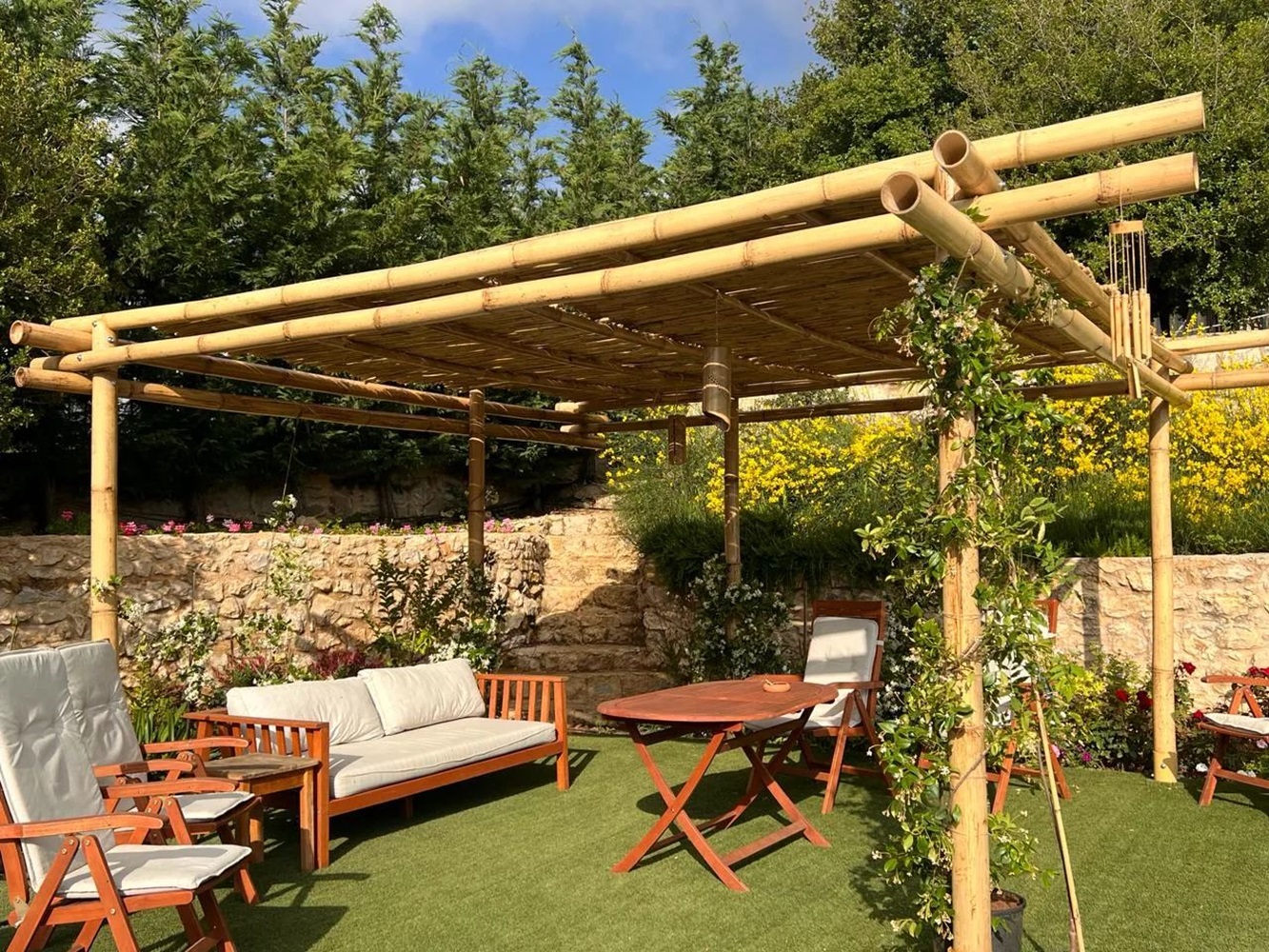 Outdoor seating area featuring a bamboo pergola, wooden furniture, and lush greenery