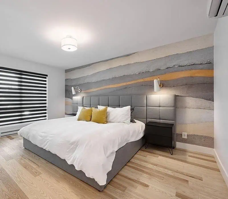 Modern bedroom with a grey upholstered bed, abstract wall mural, and striped window shades.