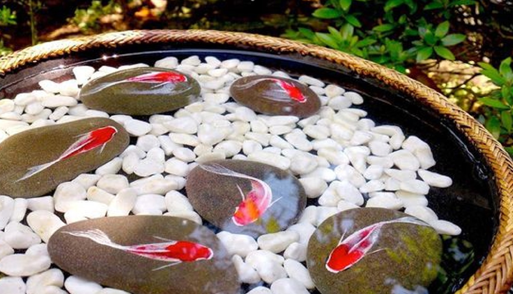 Round basket containing painted fish on stones among white pebbles in a water