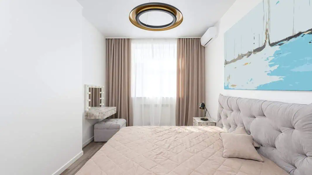 Modern bedroom with a tufted bed, beige curtains, wall-mounted makeup vanity, and contemporary ceiling light.