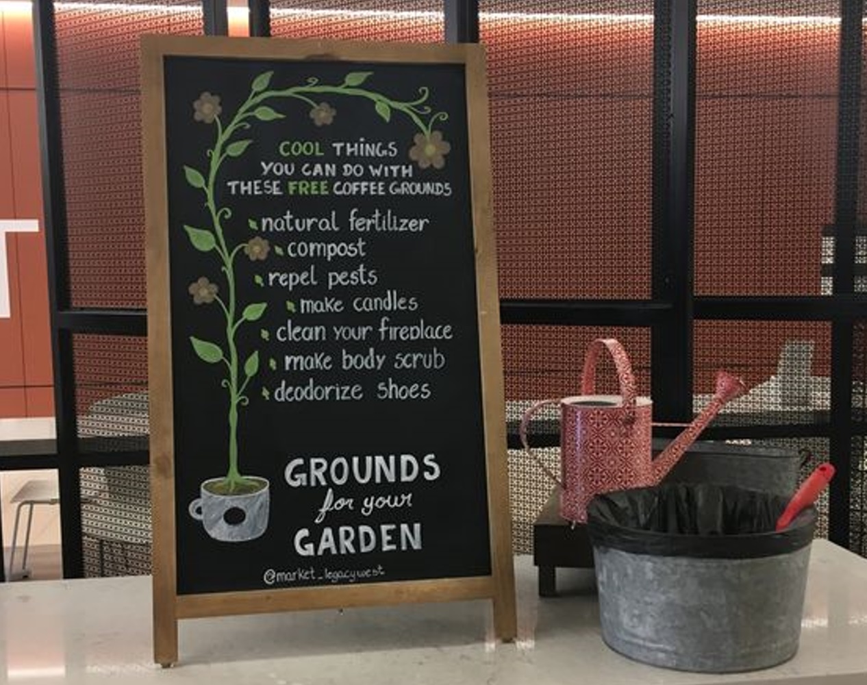 Chalkboard sign listing uses for coffee grounds next to a watering can and a bin.