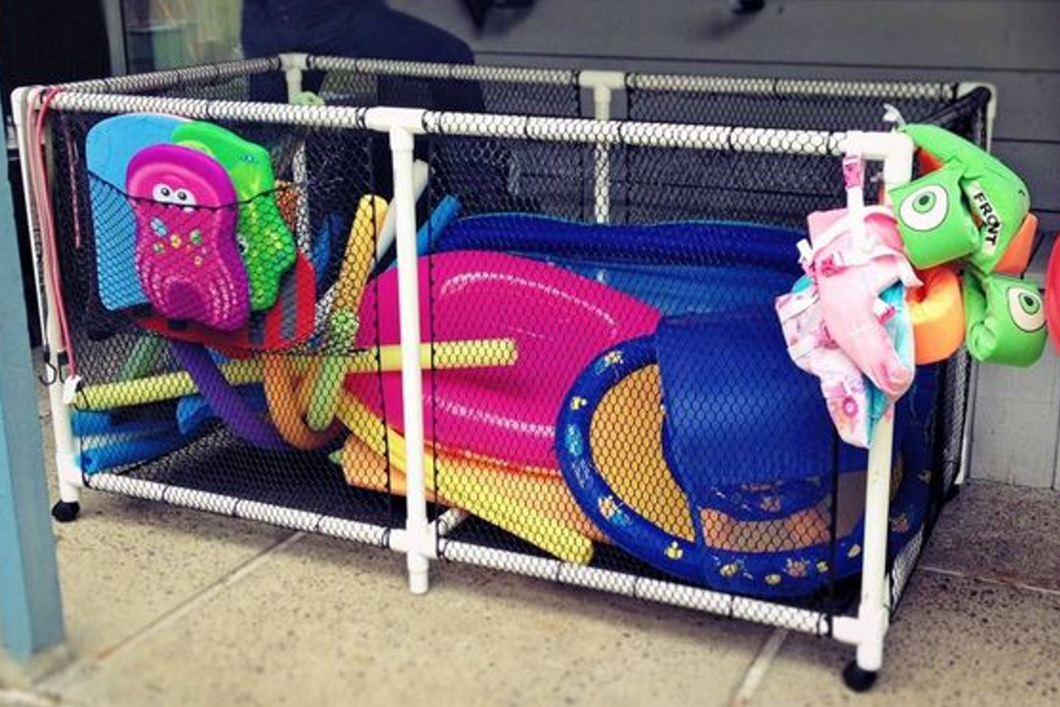 Storage bin filled with pool toys, swim noodles, life jackets, and inflatables.