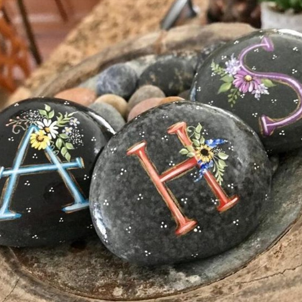 Painted stones with letters "A", "H", and "S" adorned with floral designs, perfect for DIY project