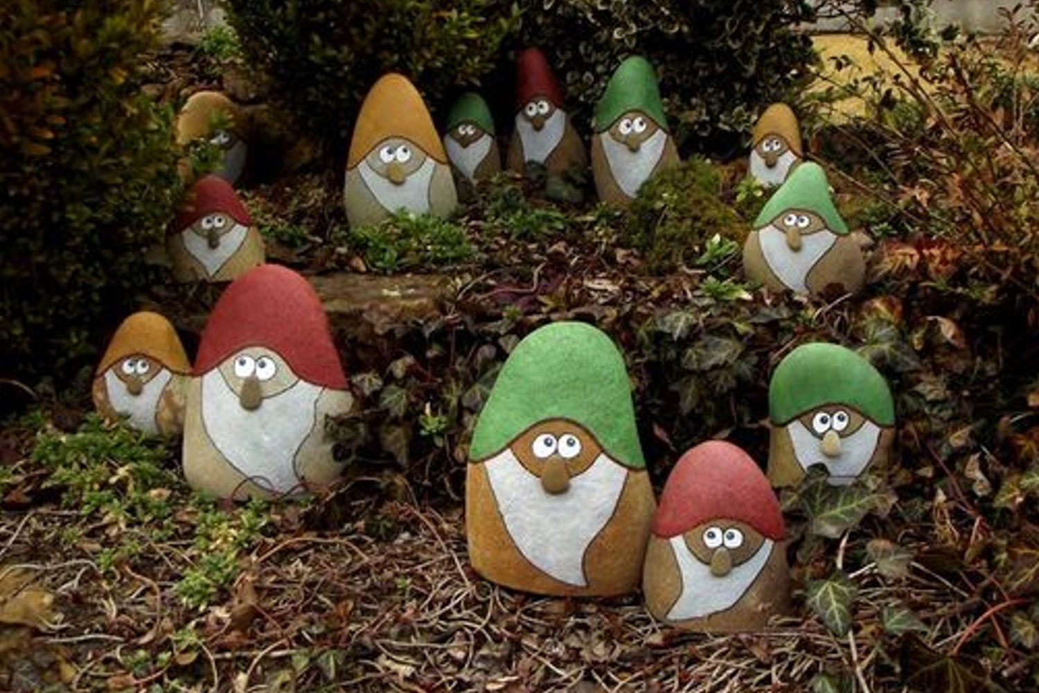 Painted stones resembling gnomes with colorful hats scattered in a garden