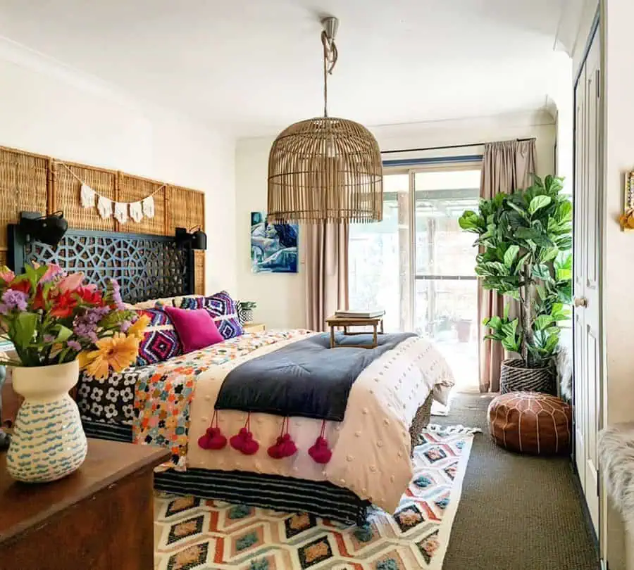 Vibrant bohemian bedroom with a colorful patterned bedding, wicker pendant light, and indoor plants.