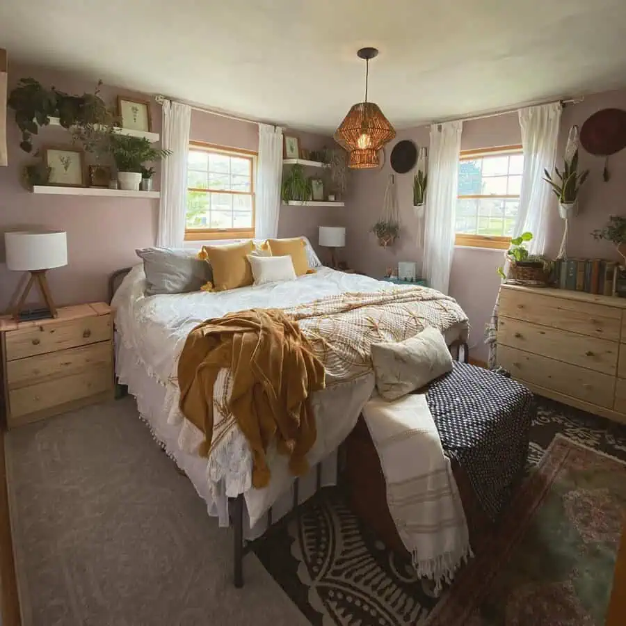 Cozy bohemian bedroom with pink walls, wooden furniture, hanging plants, and warm-toned bedding.