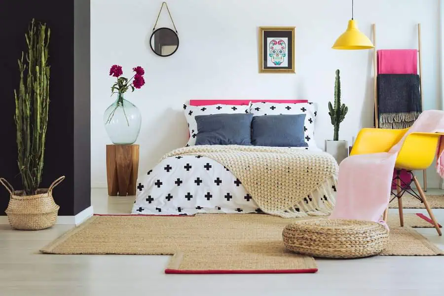 Colorful bedroom with modern decor, geometric bedding, yellow chair, and eclectic accents.