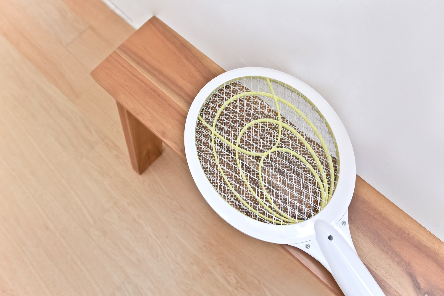 A white electric fly swatter with a yellow grid lies on a wooden bench.