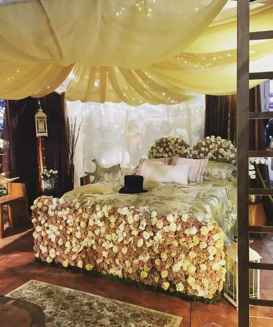 Romantic bedroom with floral-decorated bed, draped canopy, and soft ambient lighting.