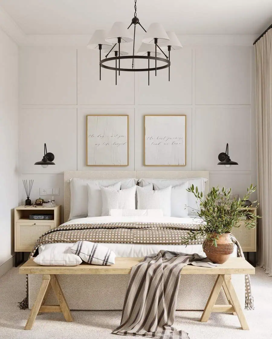 Elegant bedroom with a beige color palette, wooden bench at the foot of the bed, framed wall art, modern chandelier, and bedside wall sconces.