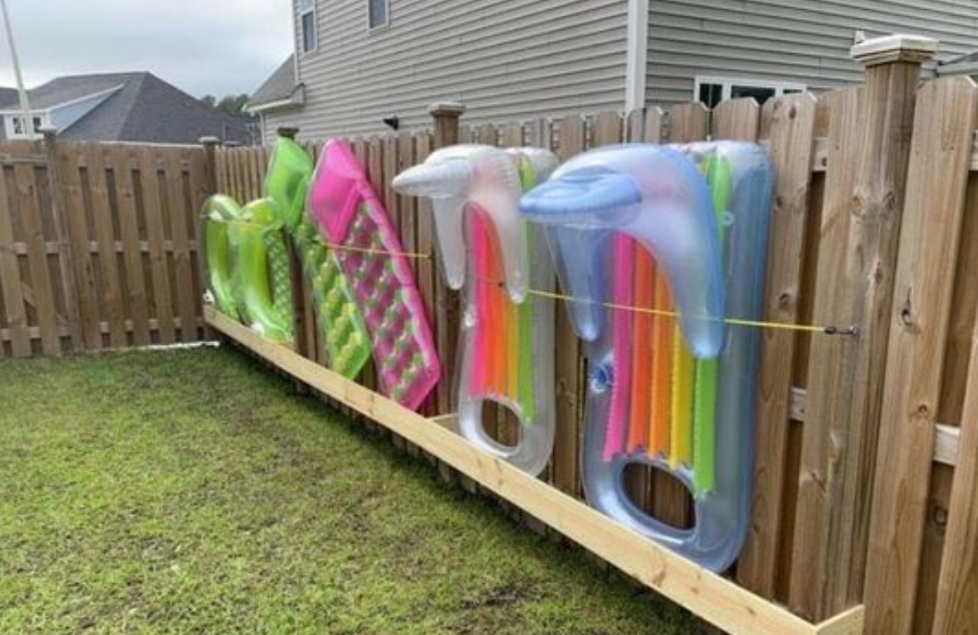 Inflatable pool floats drying on a wooden fence in a backyard.