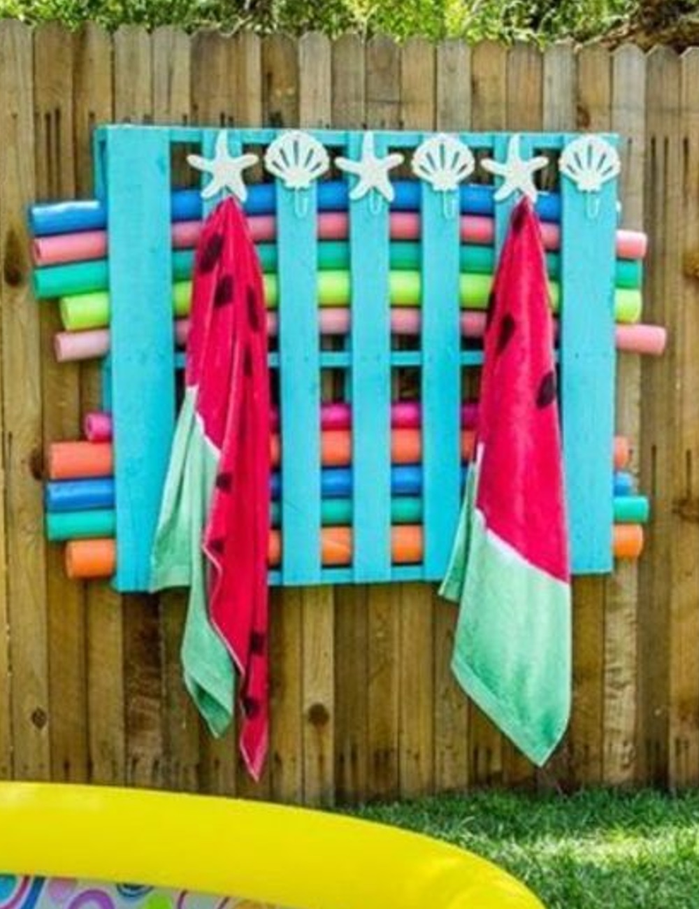 Wooden wall with colorful pool noodles and watermelon towels hanging on hooks.