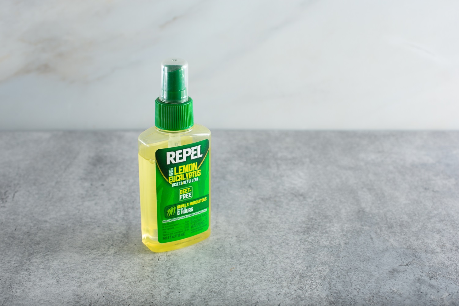 A green bottle of "Repel" insect repellent spray with lemon eucalyptus shown on a gray surface against a light background.