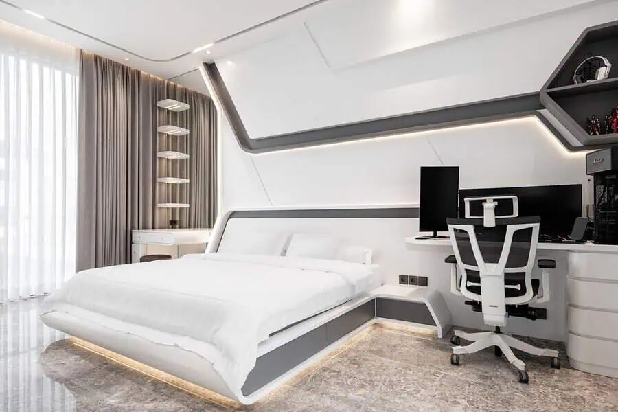 Modern bedroom with a sleek white and grey design, featuring a futuristic bed, built-in lighting, a large desk with a computer setup, and floor-to-ceiling curtains.