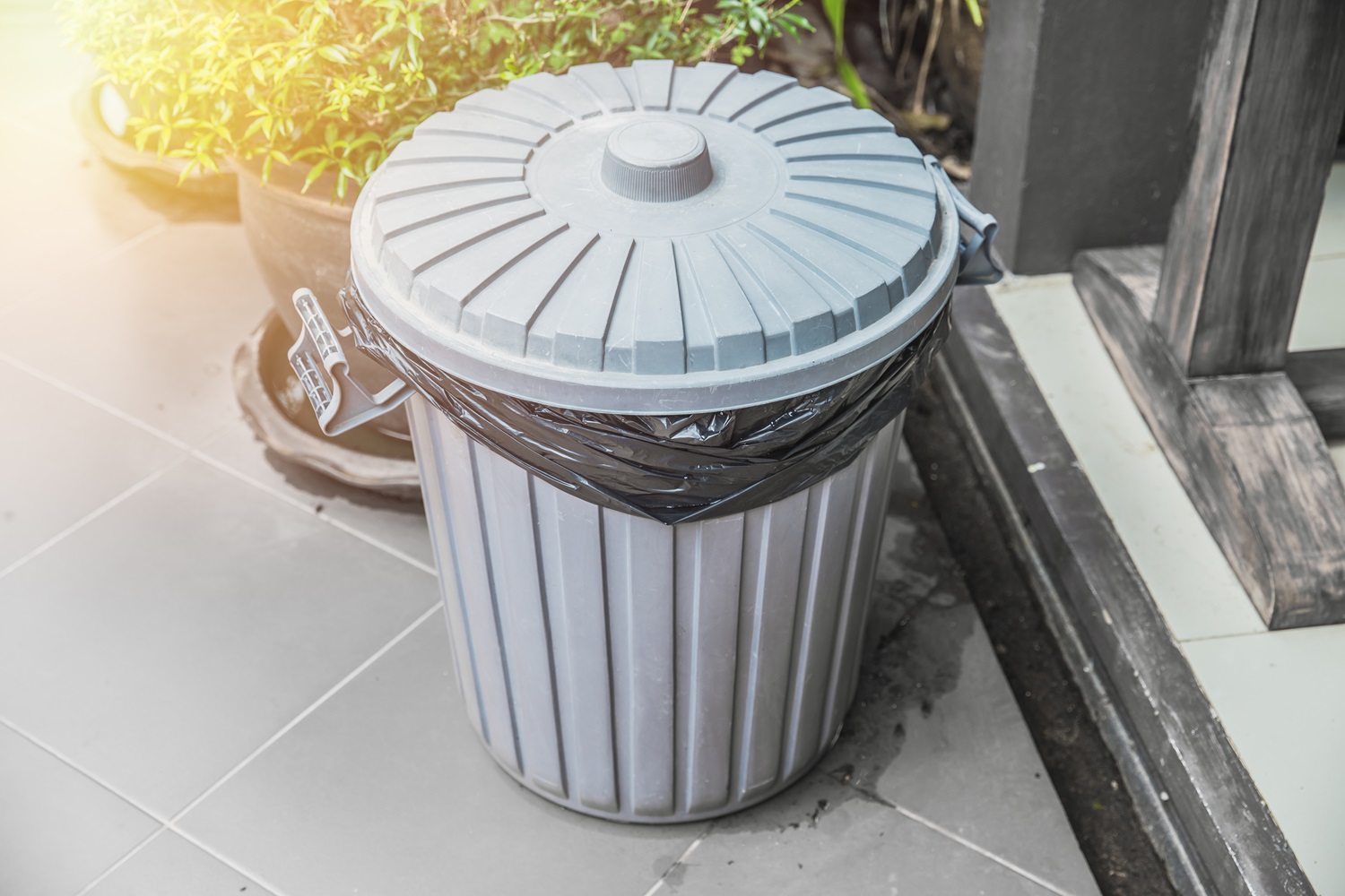 A gray plastic trash bin with a black garbage bag liner.