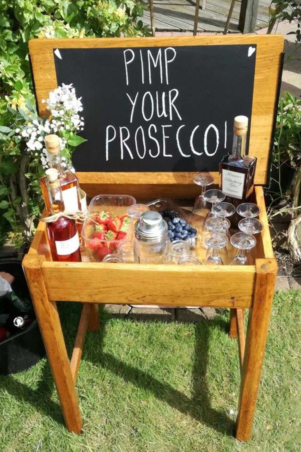 A wooden table with prosecco bottles, fruits, and glasses under a sign "Pimp Your Prosecco.