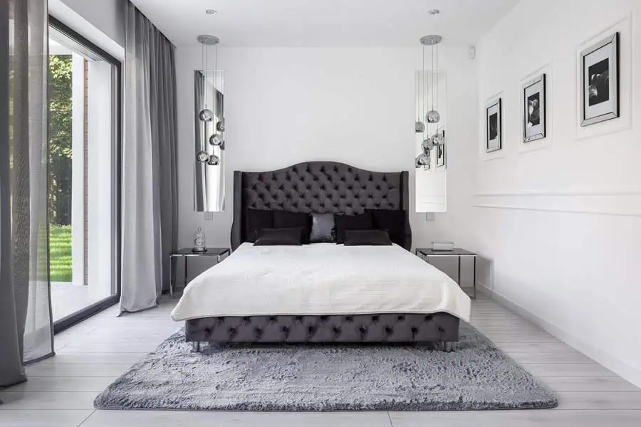 Contemporary bedroom with tufted dark grey bed, monochromatic decor, and large windows with grey curtains.