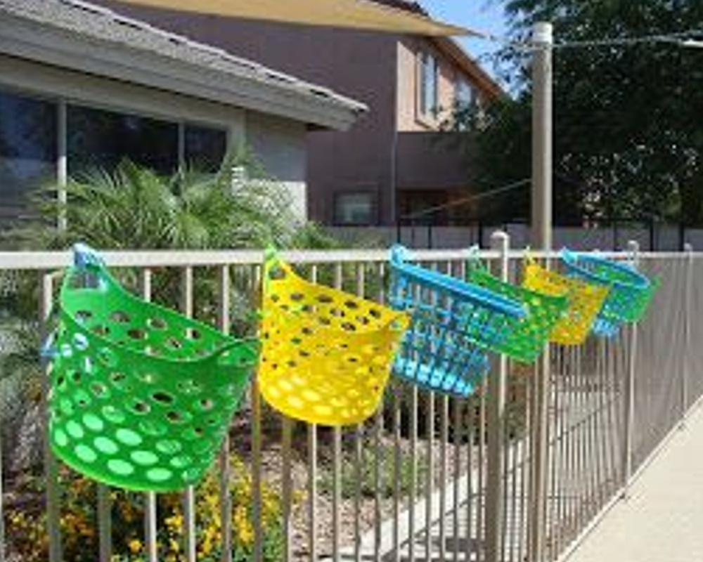 Colorful plastic baskets hanging on a metal fence in a sunny outdoor setting.