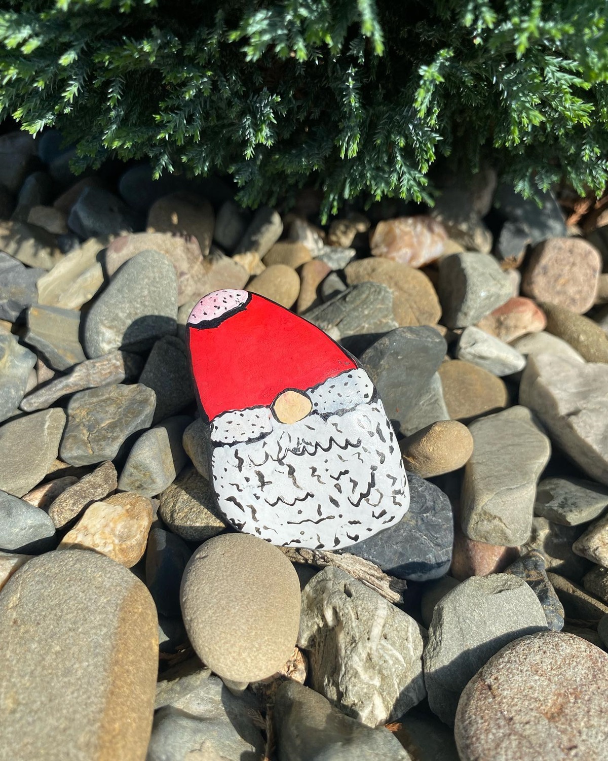 Painted rock of a gnome with red hat and white beard placed among garden stones