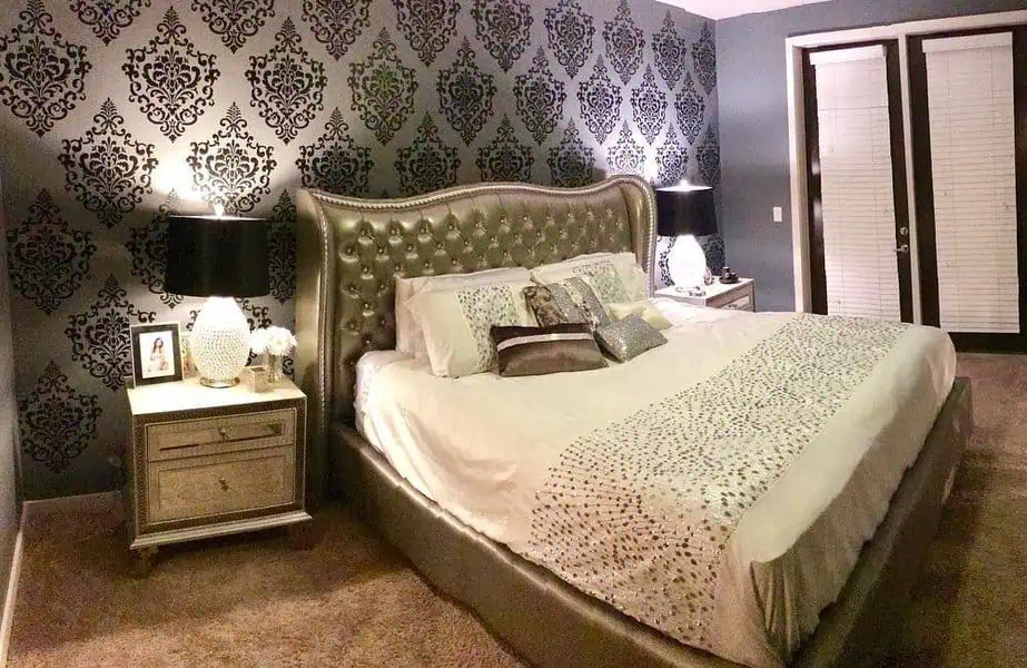 Elegant bedroom with silver tufted bed, damask wallpaper, and matching bedside tables.