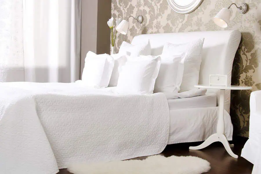 Chic bedroom with white bedding, damask wallpaper, and modern white side table.